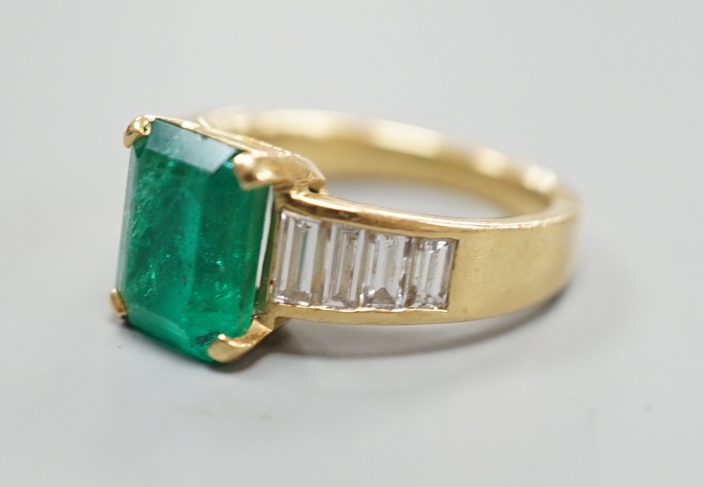 A modern yellow metal and single stone emerald set dress ring, with graduated baguette cut diamond set shoulders, size M/N, gross weight 7.3 grams.